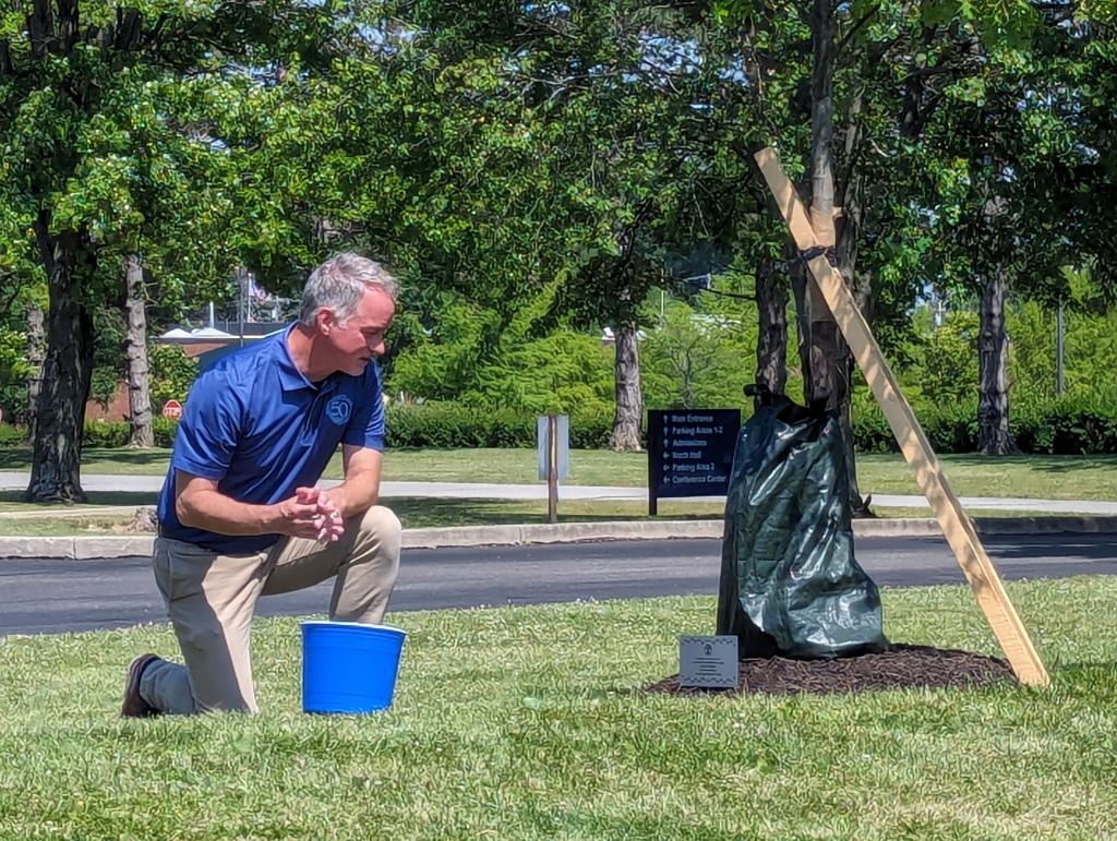 President Chris Spradlin reads a plaque dedicating a newly planted tree during the College’s Tree Ceremony