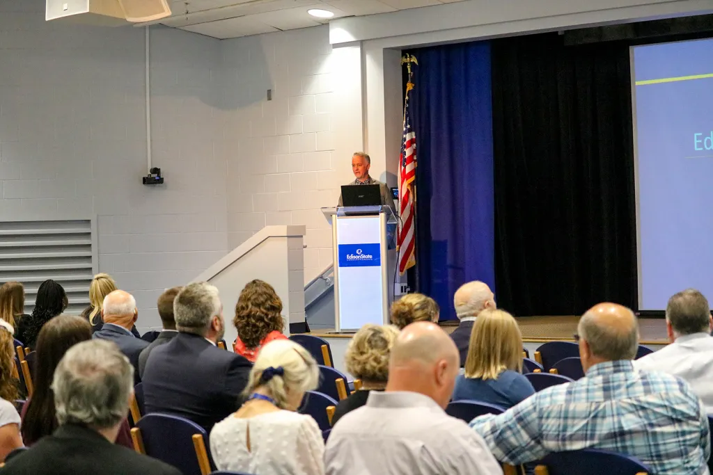 President Chris Spradlin speaks at a podium during the annual State of the College address while attendees listen from the audience.
