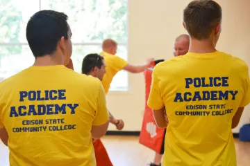 Police Academy program participants wearing yellow academy shirts engage in hands-on defensive tactics training