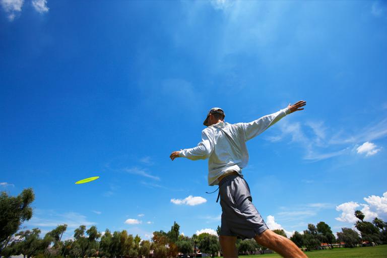 Person throwing a disc golf, sunny skies, trees