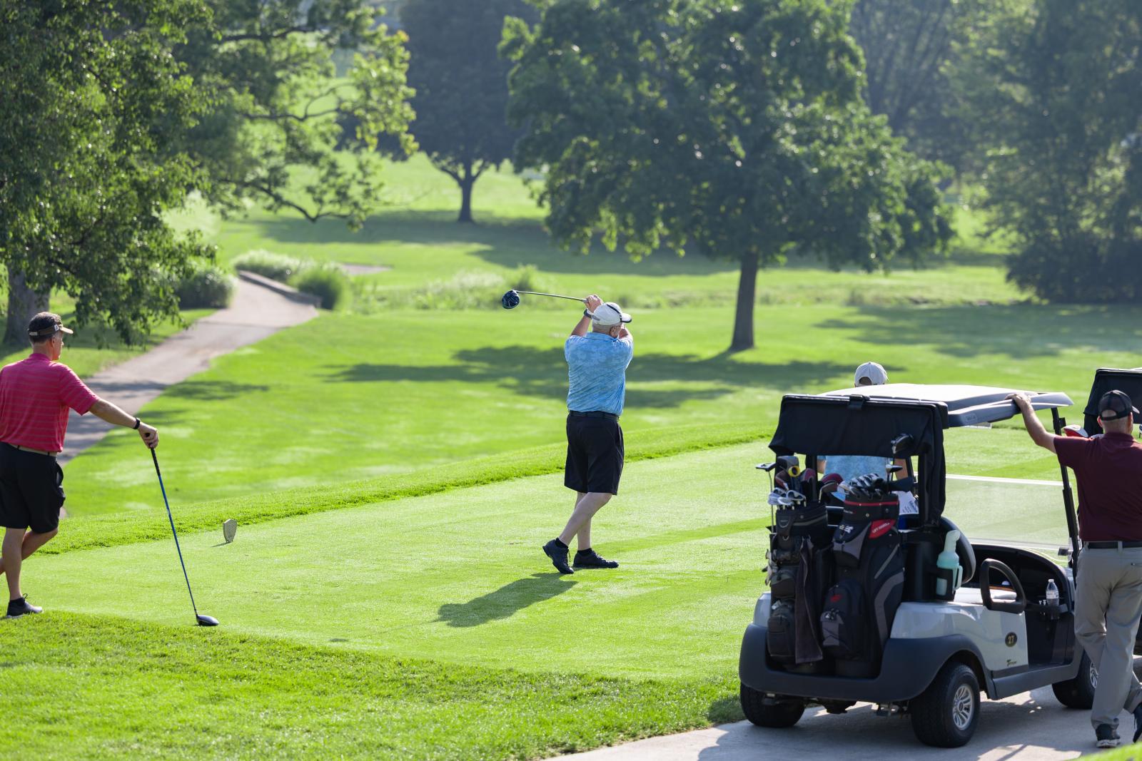 Man in blue shirt swings golf club at country club