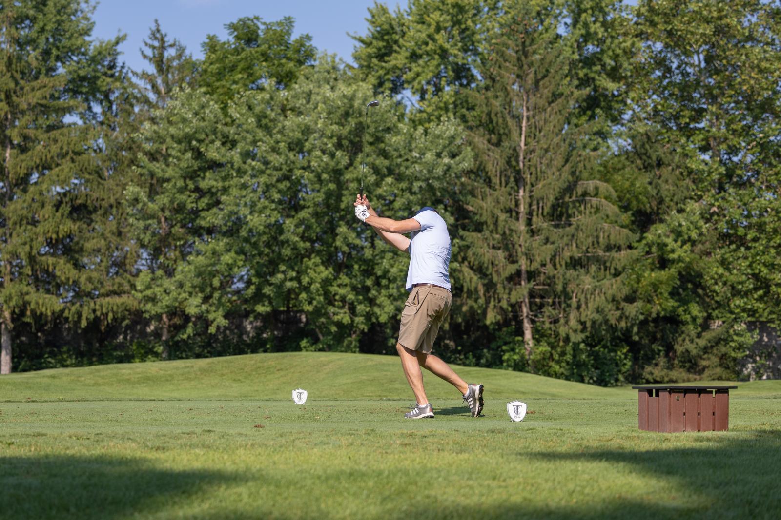 Golfer swings golf club on green field with trees in background