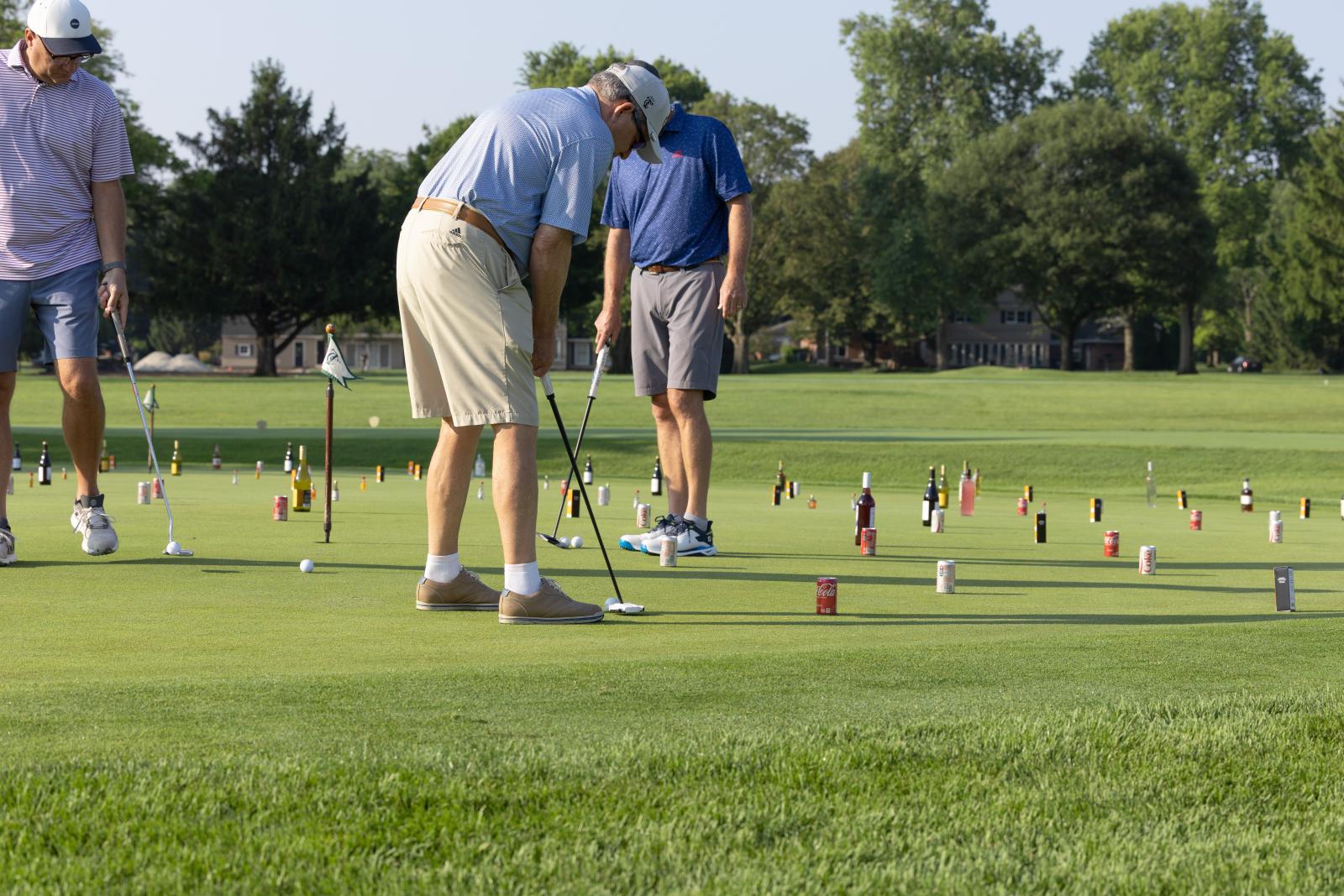 Men putting golf balls around bottled drinks in a game