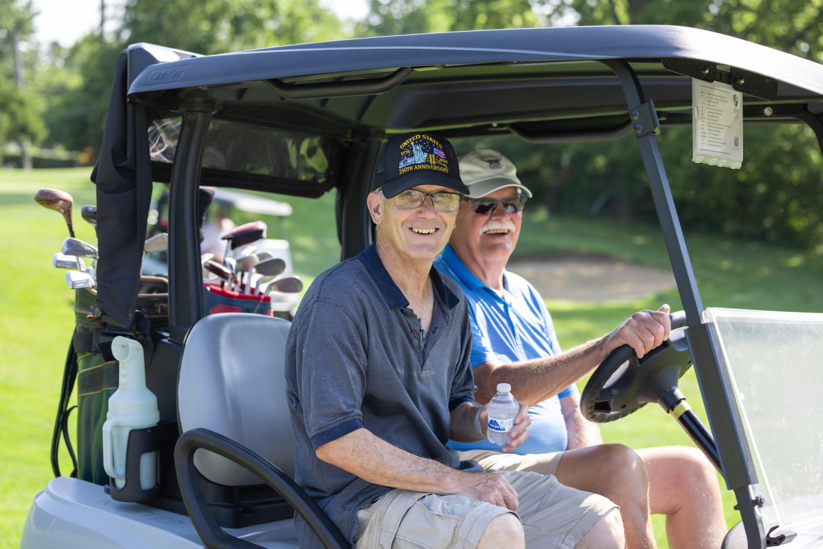 Two men smiling while riding in a golf cart